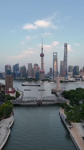 Aerial footage moving over the Waibaidu Bridge on Suzhou Creek, revealing the Pudong skyline with its iconic skyscrapers and the Huangpu River under a clear sky in Shanghai, China.