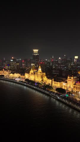 Aerial footage showcasing the illuminated historical buildings of the bund along the huangpu river against the modern Shanghai city skyline under a dark night sky, China.