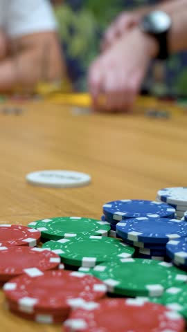 Poker chips in foreground with playing cards and hands in background, casino gambling game and betting entertainment concept