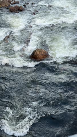 Close up view of fast river rapids in Lyngdal, Norway with whitewater foam flowing over dark rocks, showing powerful Nordic nature.