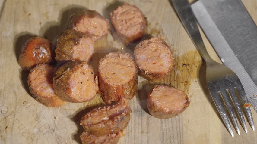 Extreme close-up of chopped roasted pork sausage pieces with rising steam, Macro shot of steaming hot sliced grilled chorizo sausage on a wooden board