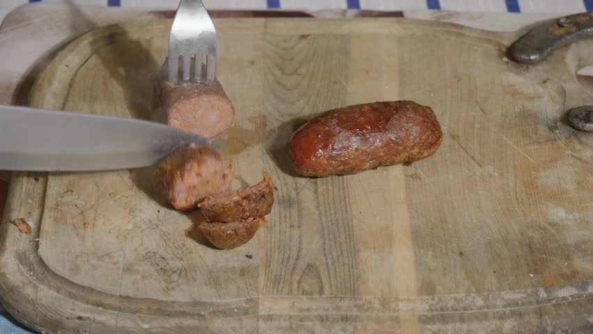 Close-up of slicing steaming hot grilled chorizo sausage on a wooden board
