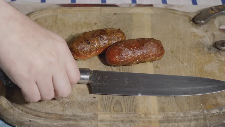 Slicing freshly grilled pork sausage on a wooden cutting board close-up