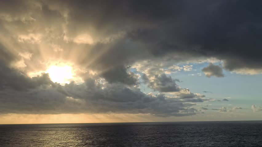 At Sea - A seascape captures sunlight filtering through dramatic clouds above the ocean.