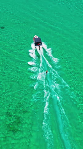  A drone view of a guy skiing behind a speedboat on crystal-clear water. Extreme sports, recreational activities