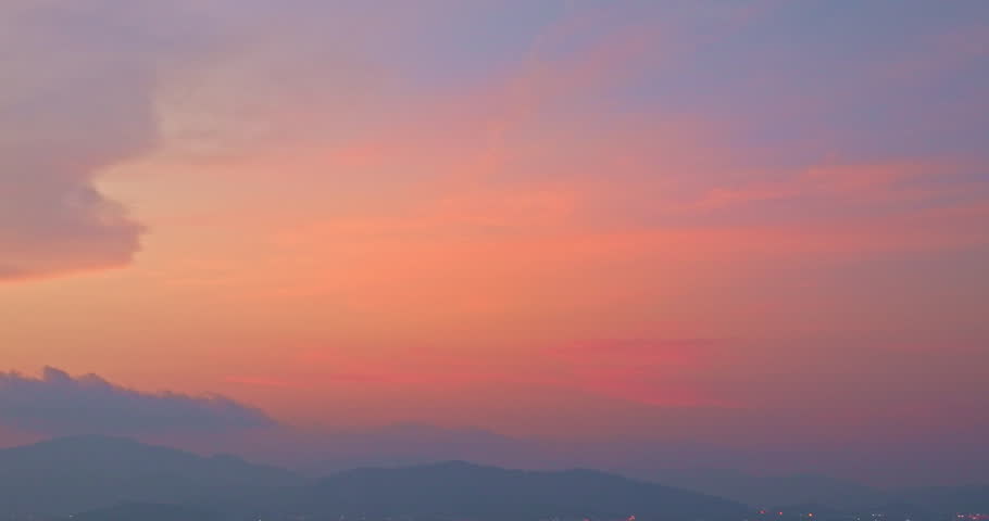 A stunning scene of a vivid sunset with pink and orange hues illuminating the sky over a tranquil rocky shoreline. The silhouetted mountains and serene water create a peaceful and atmospheric view