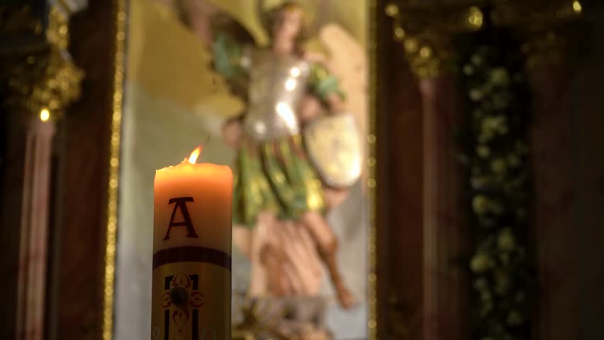 Interior of a church, with the religious figure in the background and a lit candle in the foreground.