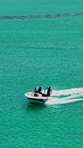  A drone view of a guy skiing behind a speedboat on crystal-clear water. Extreme sports, recreational activities