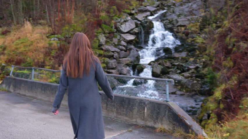 Woman Admiring Cascading Waterfall from Forest Bridge