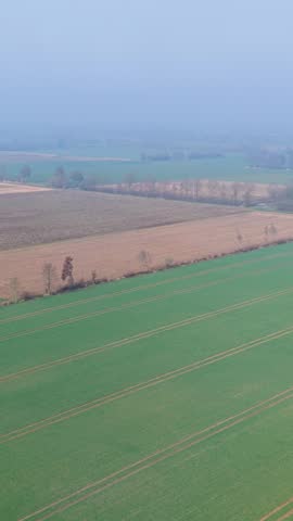 An aerial high angle view shows vast agricultural fields and farmlands stretching into a hazy horizon Patches of green grass and brown cultivated soil create geometric lines across the rural landscape