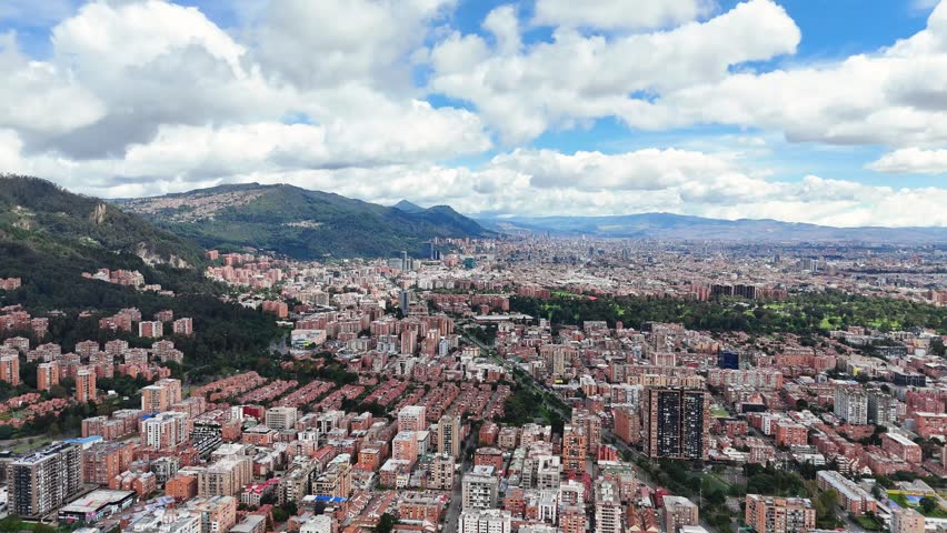 A sweeping view of Bogotá illustrates numerous high-rise buildings nestled against the lush backdrop of mountains, showcasing city life.