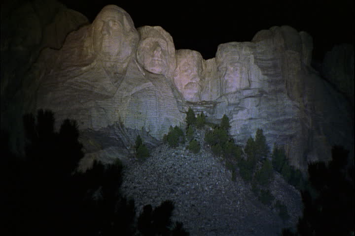 Mount Rushmore illuminated by white light at night in Keystone, South Dakota.