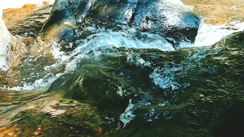 High angle close up of rapid water rushing over dark wet stones, crystal clear river current texture, dynamic splashing stream in the woods, natural fresh water flow background.