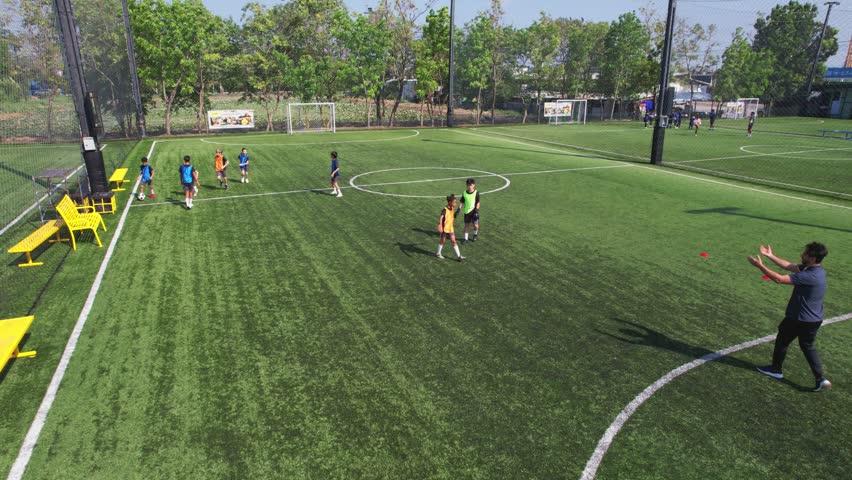 Aerial view of children practicing football on outdoor field with coach. Group of young active kid players practicing soccer skill and teamwork with trainer support during outdoor training activity.