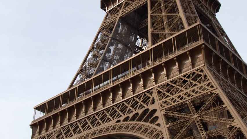 A low angle camera pans up the iron lattice structure of the Eiffel Tower