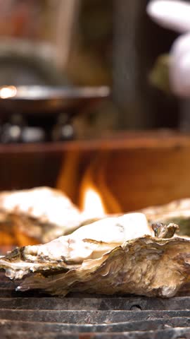 Close-up shot of large oysters cooking on a grill with flames at a Tokyo market.
