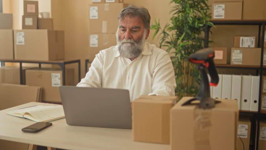Man with packages stretches arms behind head in a building office near laptop and parcel scanner; business productivity relief.