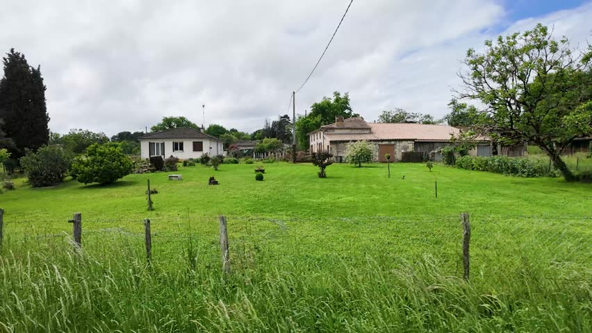 Wide panning shot of a lush green backyard garden and traditional stone farmhouse in France