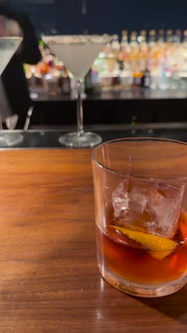 Close-up shot of a whiskey cocktail with orange peel on a wooden bar counter
