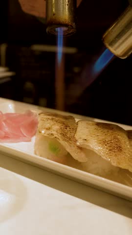Close-up shot of a chef searing fresh nigiri sushi with a blue blowtorch flame