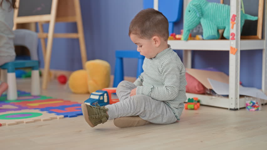 Little boy kneeling and playing with a toy truck, hands visible on foam mat in a preschool building; concentration exploration.