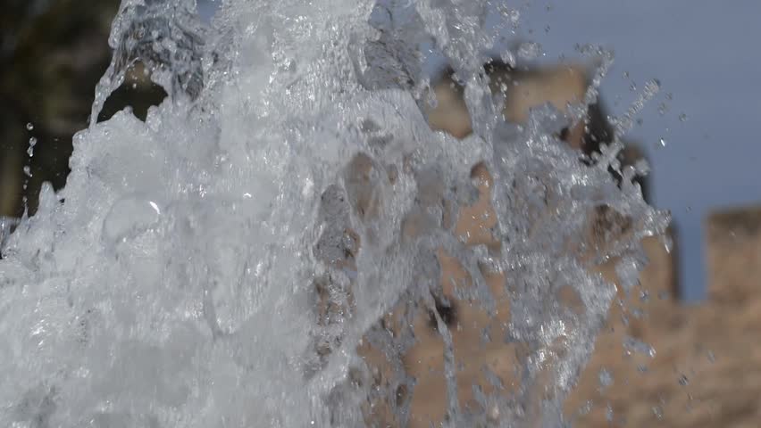 Super slow motion of a fountain jet with the blurred medieval walls of the Altamira palace in the background. Elche, Spain.