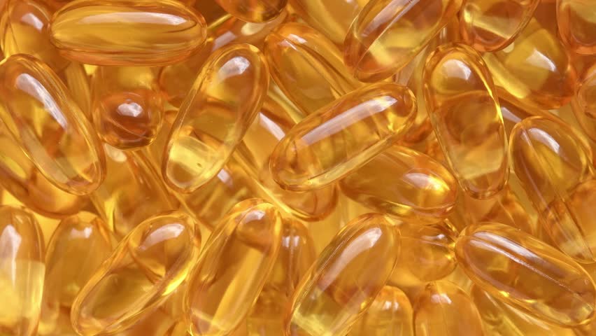 Amber soft gel capsules rotate slowly in macro closeup for supplement, healthcare, pharmacy and wellness advertising concepts