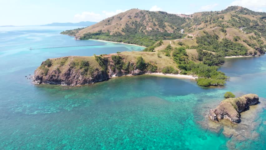 Aerial view of the northern headland near Labuan Bajo in Komodo National Park, Indonesia, surrounded by vibrant coral reefs and turquoise tropical waters under a sunny blue sky