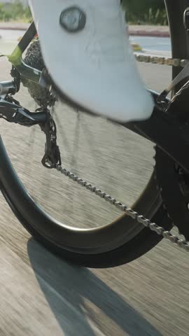 Professional male road cyclist riding bicycle in morning sunlight, close up of legs and bike wheel. Bike gear, chain and cassette rotation. Vertical video