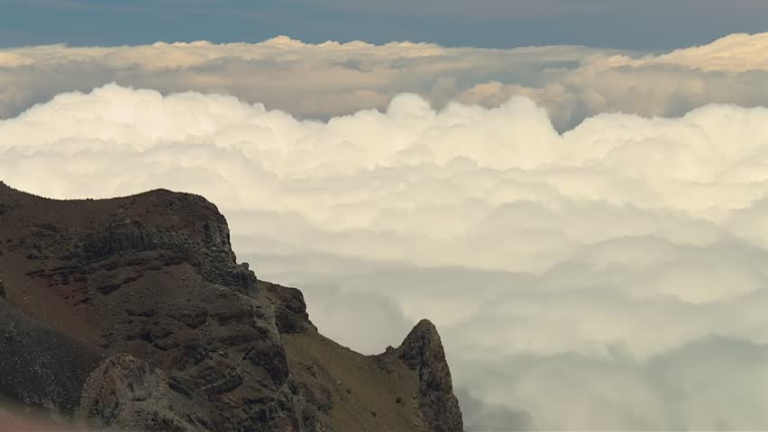 Breathtaking static footage of rugged volcanic cliffs at Haleakala National Park rising above a vast sea of clouds under soft daylight, showcasing dramatic terrain and sweeping sky vistas.