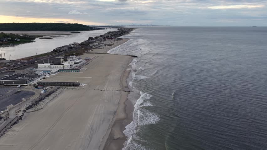 A view of the Sea Bright, New Jersey beach showing the Atlantic Ocean and the Shrewsbury River in late spring around sunset. The New York City skyline is visible at a distance.