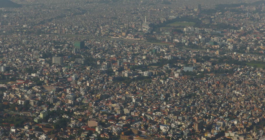 Aerial view of Kathmandu Valley Nepal featuring dense urban landscape beneath snow capped Himalayan mountains during clear daylight with atmospheric haze and expansive city scenery