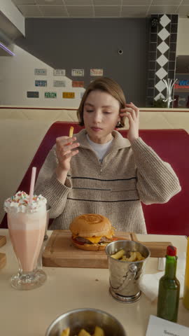 Medium vertical POV of young Caucasian student girl speaking with excitement and agitation while enjoying tasty burgers with friends after passing college exams at fast food diner