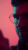 Close-up shots of a young man wearing round glasses with expressive emotions under dramatic red and teal lighting, showcasing a contemplative and then smiling facial expression - Powered by Shutterstock - Get 15% off with code: PIKWIZARD15