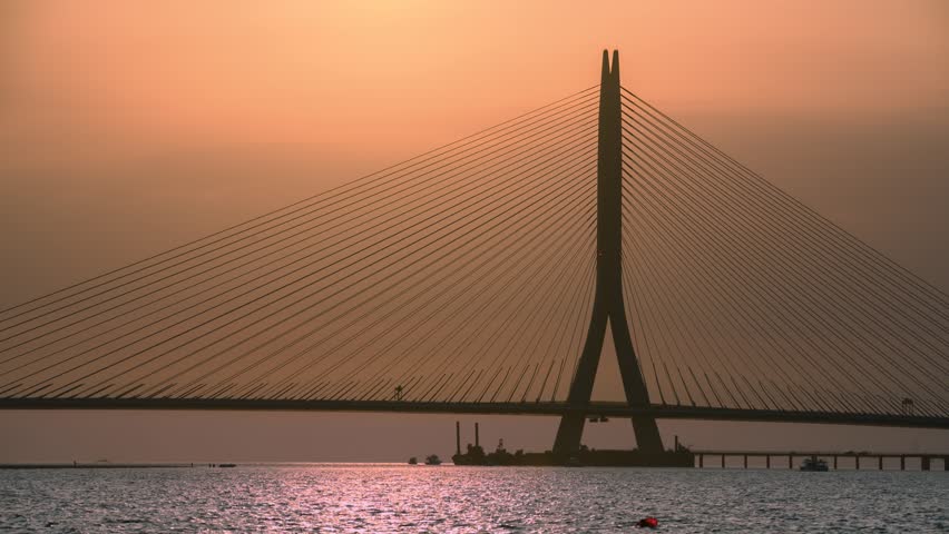 A scenic sunset view of the iconic Danjiang Bridge in Tamsui, New Taipei City, Taiwan, featuring the cable-stayed structure silhouetted against the sun.