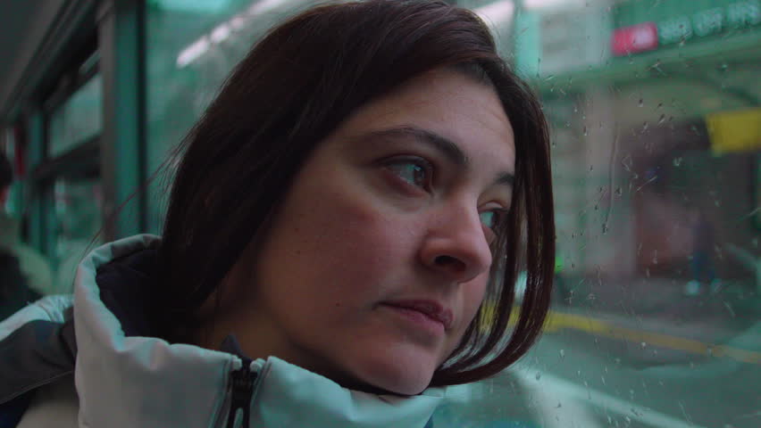 Female passenger gazes outside public transport with raindrops on glass suggesting introspection solitude and reflective everyday journey experience