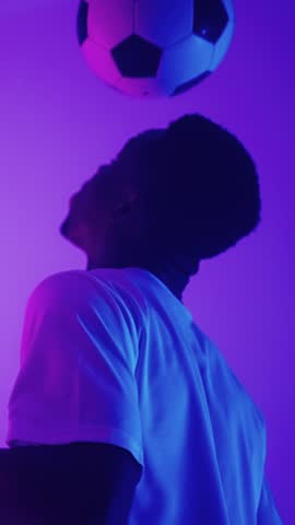 Dynamic portrait of a football player skillfully balancing a soccer ball on his head under vibrant purple and blue lighting, showcasing agility and concentration in sports practice