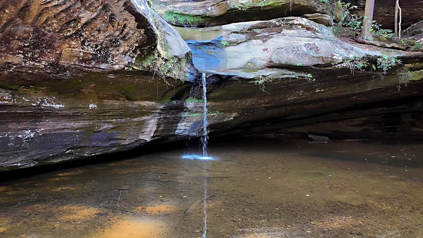 View of a small waterfall flowing over layered sandstone rocks into a pool at Hocking Hills State Park, Logan, Ohio, United States.