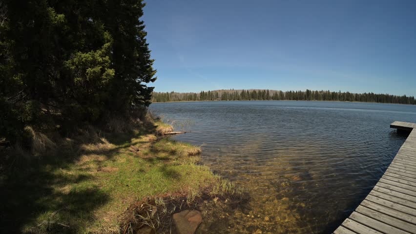 Wide angle view of a small northern lake and wooden dock under a blue sky with small waves on the water