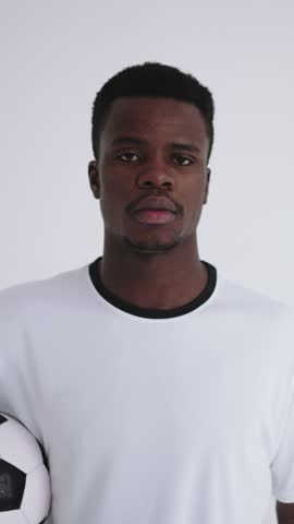 Portrait and full body shots of a focused male football player in plain white sportswear holding and standing with a classic black and white soccer ball against a minimalist white background