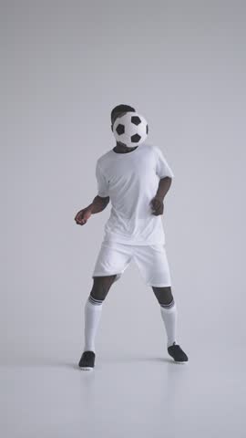 Young male football player dressed in white sportswear skillfully controlling and juggling a classic black and white soccer ball in a minimalistic studio setting