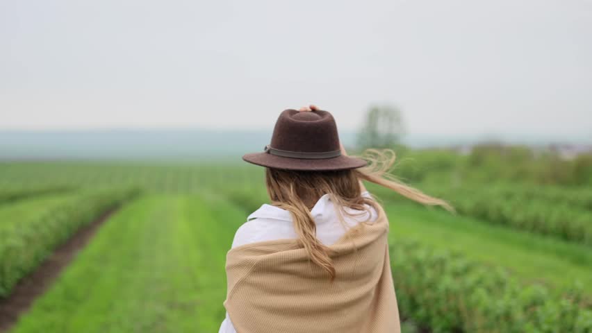 Woman walking through green agricultural field wearing a hat