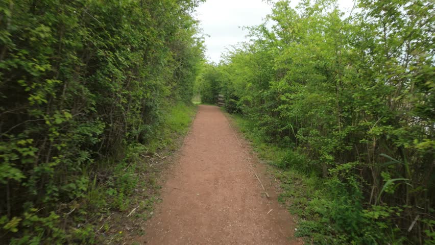 Crown Lakes Country Park, Peterborough, England, UK - May 21 2026: Walking along a footpath toward an opening and around a corner on a bright spring morning with everything in bloom.