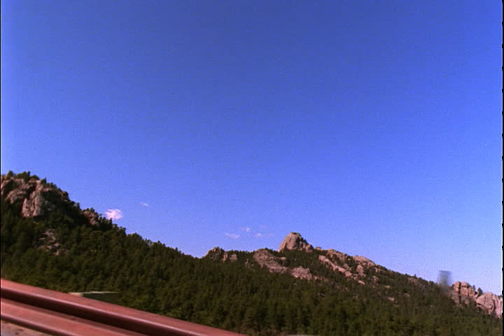 The Black Hills seen out window of moving car on the road to Mount Rushmore, passes sign for parking in Keystone, South Dakota.