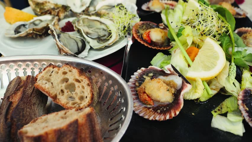 Table in a French restaurant with sea scallops, fresh oysters, salad, and a basket of baguette. Elegant fine dining seafood meal. High quality 4k footage