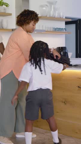 Vertical video: Grabbing backpack mom in kitchen fixing braid and strap, sending kids to school. Parent, children, morning, home, breakfast, caregiving, vertical video