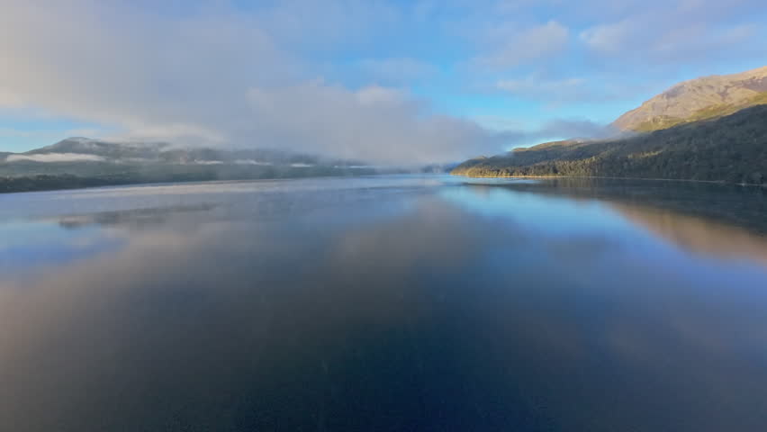 FPV Drone Flying Over Lake Towards Misty Mountains