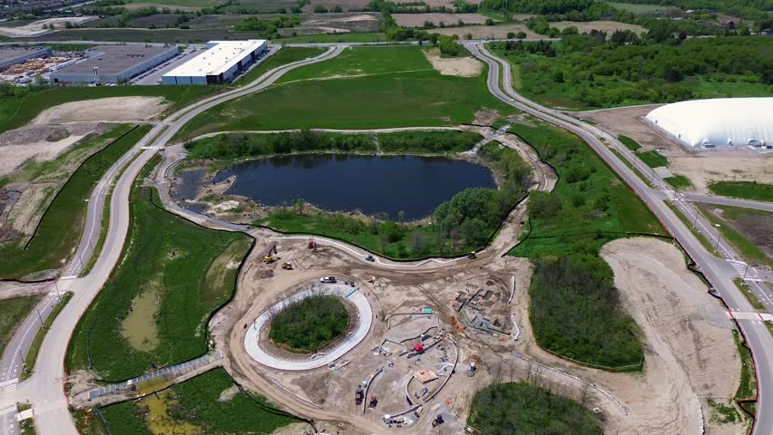 Drone aerial view of a roundabout and roadway construction project near North Maple Regional Park in Vaughan Ontario. Urban development area with stormwater pond, newly built roads, and expanding suburban neighborhood on a sunny day in Canada. Vaughan, Canada - May 26, 2026.