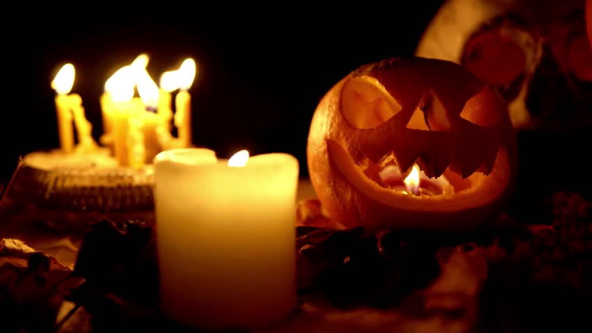 Cute creepy two pumpkins standing on heads with scary face carved out, glowing from inside, surrounded Halloween decorations, flickering candles, cold