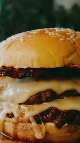 Massive double decker bacon cheeseburger with melted cheese and natural light background. Juicy stacked burger with rich texture and dripping ingredients.